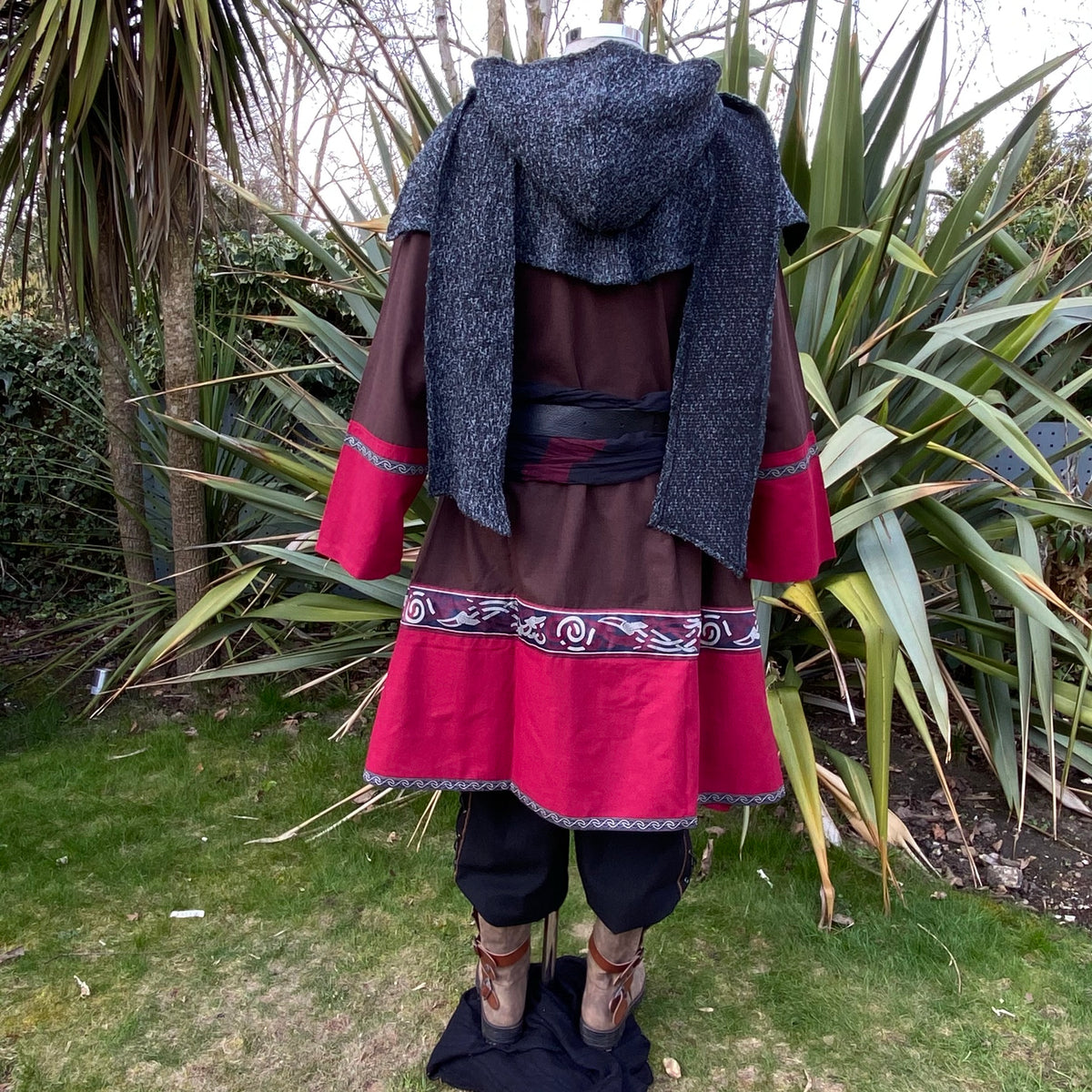 Medieval LARP back view: red-brown tunic, draped mantle, ornate belt.