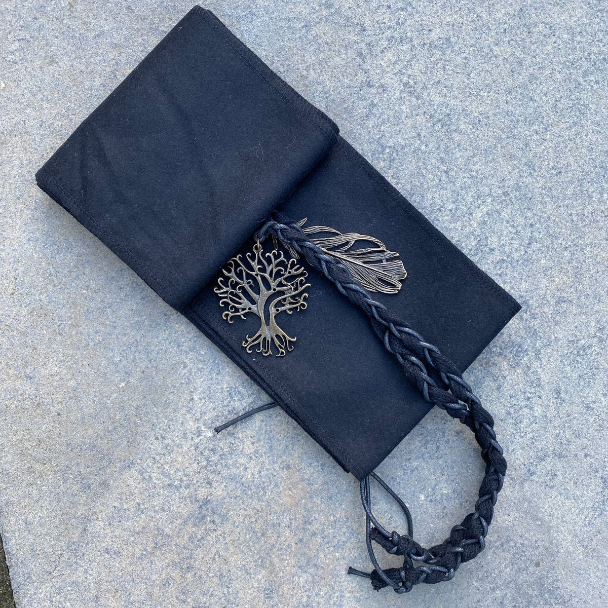 Braided LARP sash with tree and feather pendants on stone background.