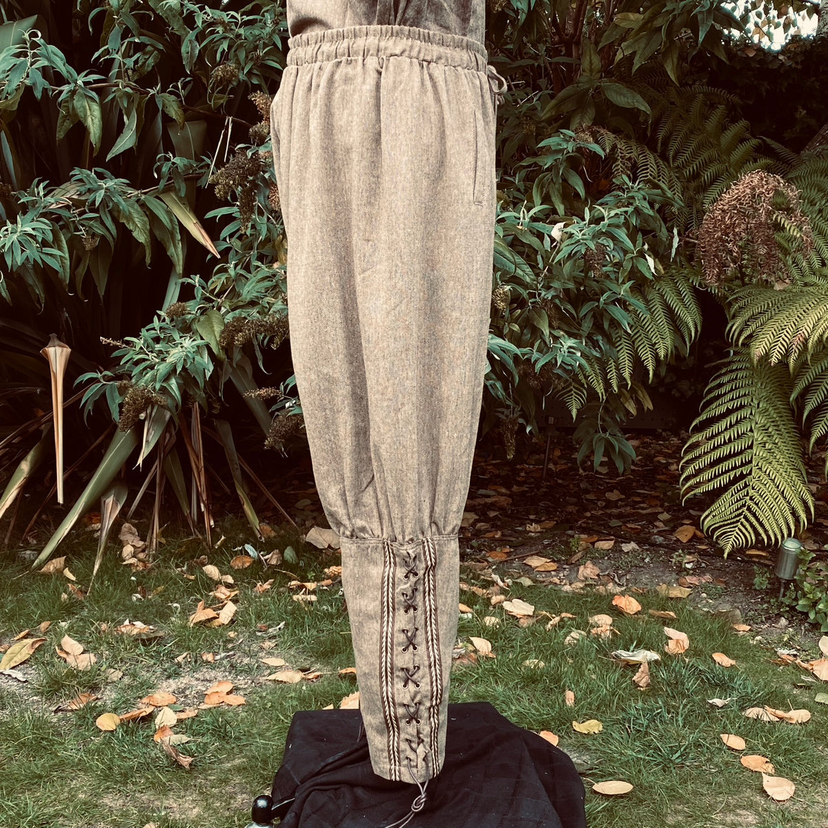 Medieval LARP beige pants with side lacing, garden backdrop view.