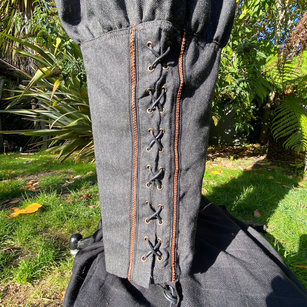 Close-up of woven braiding and crossover calf lacing on grey wool Viking trousers.