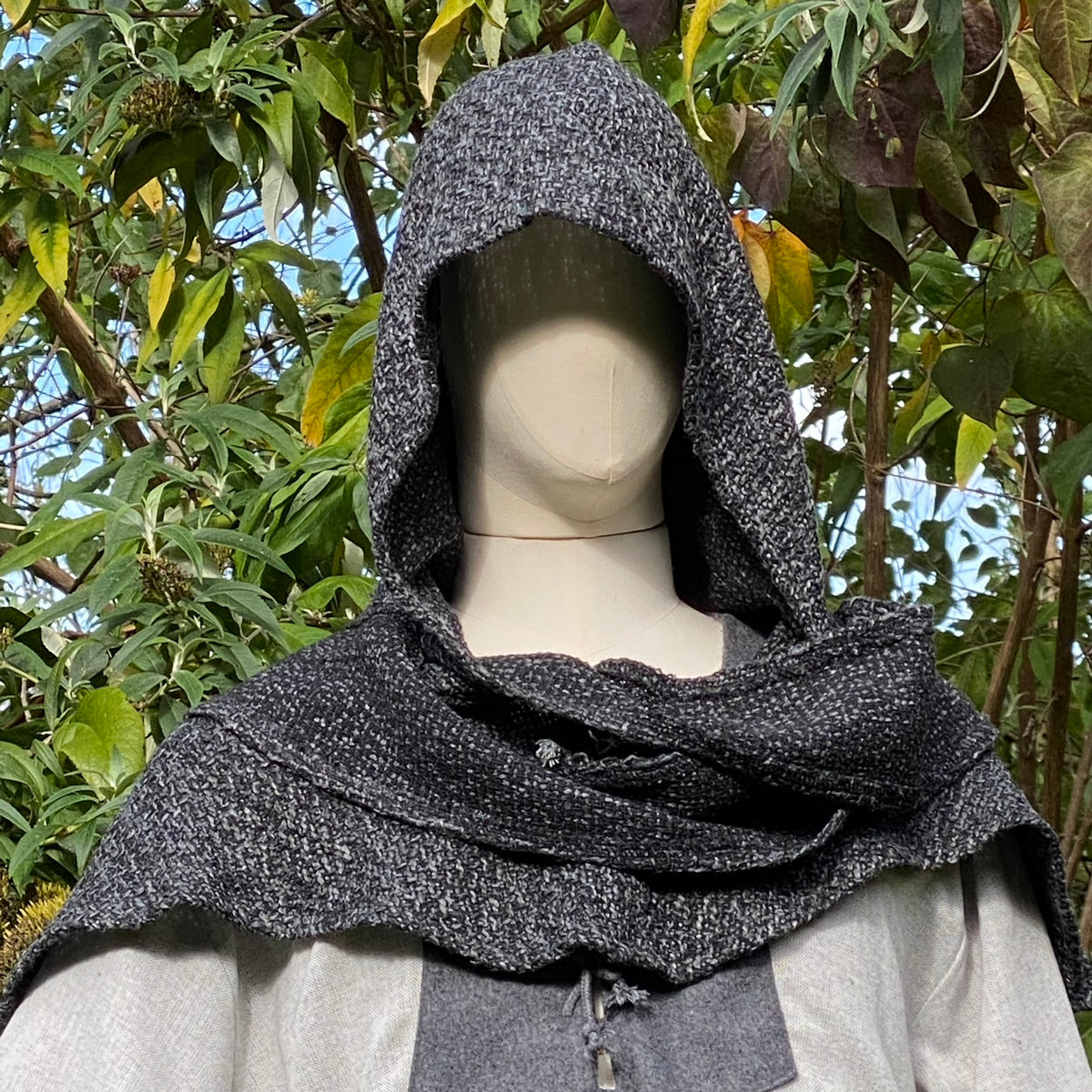 Close-up of LARP medieval hooded tunic, textured fabric with foliage backdrop.