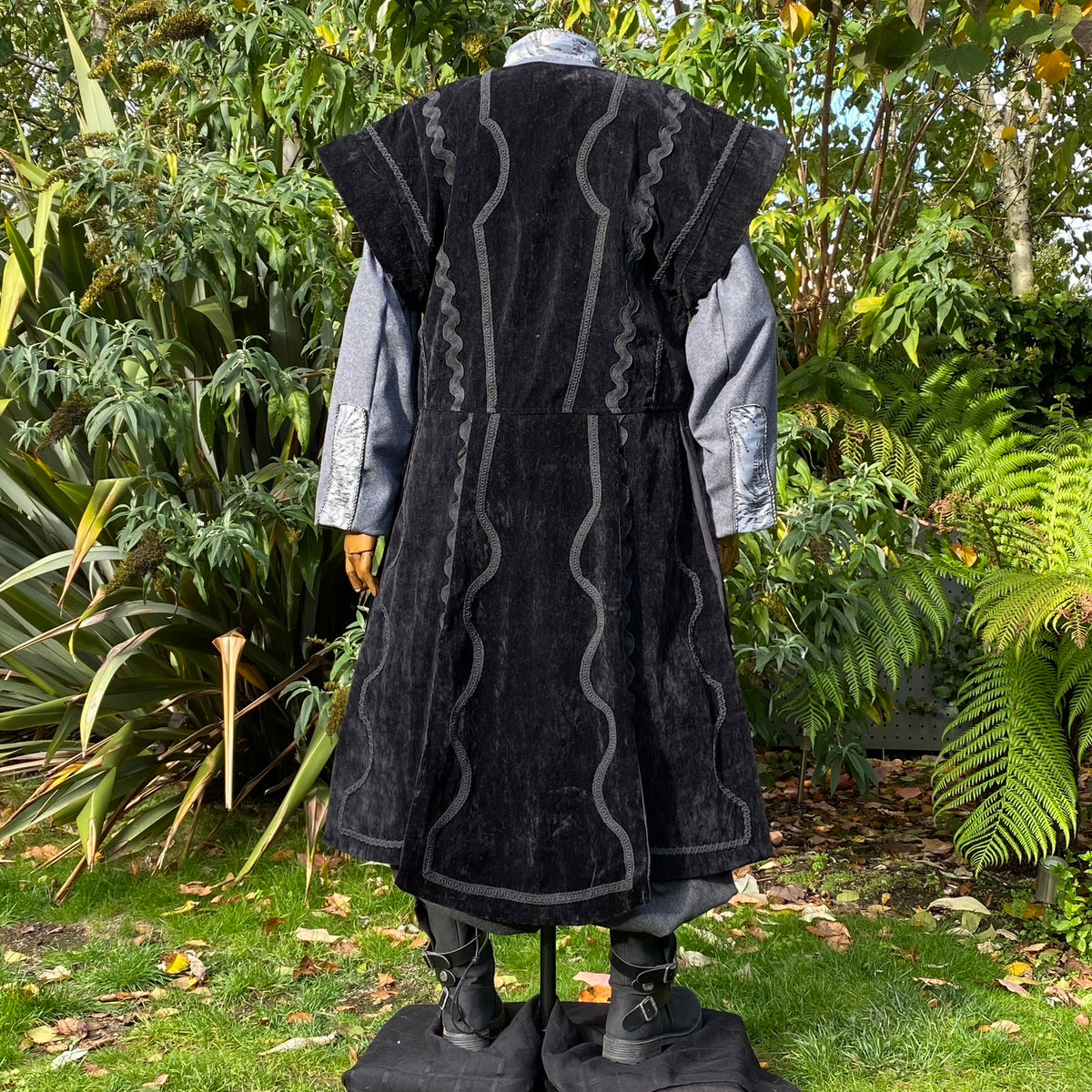 Black medieval-style waistcoat with wavy trim, over grey shirt, back view.