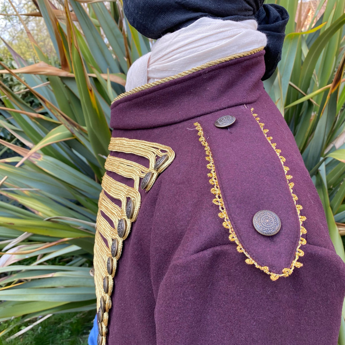 Maroon pirate coat with gold trim detail, side garden view, for LARP events.