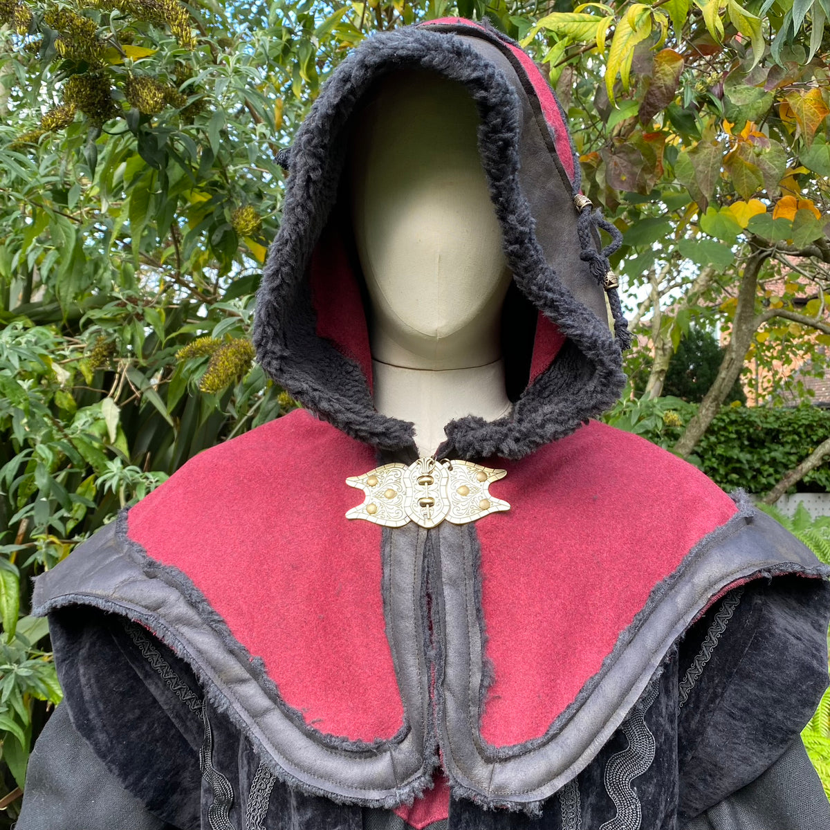 Mannequin wearing medieval LARP hood, red and black fleece, ornate clasp.