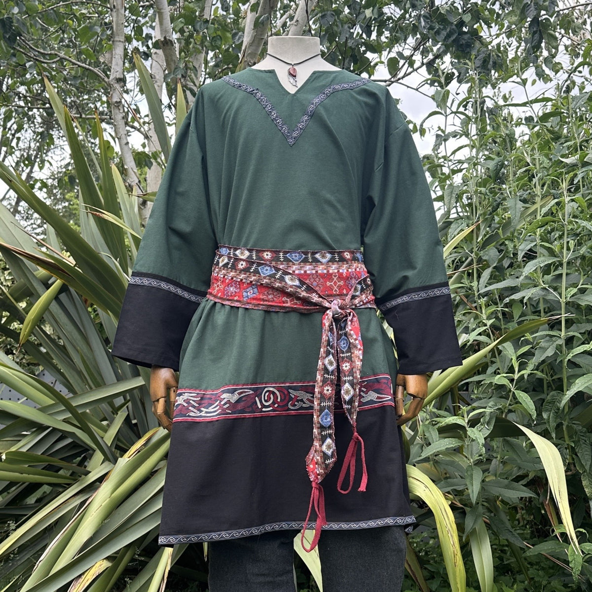 Green and black medieval tunic with red patterned belt, front view.