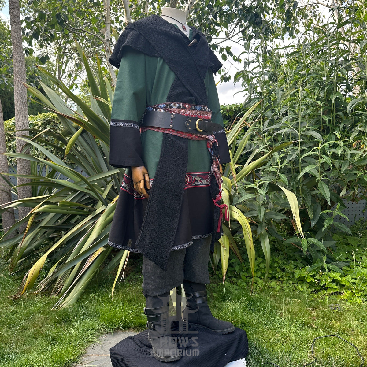 Medieval LARP costume side view featuring a green and black tunic, wool hood, trousers and sash.