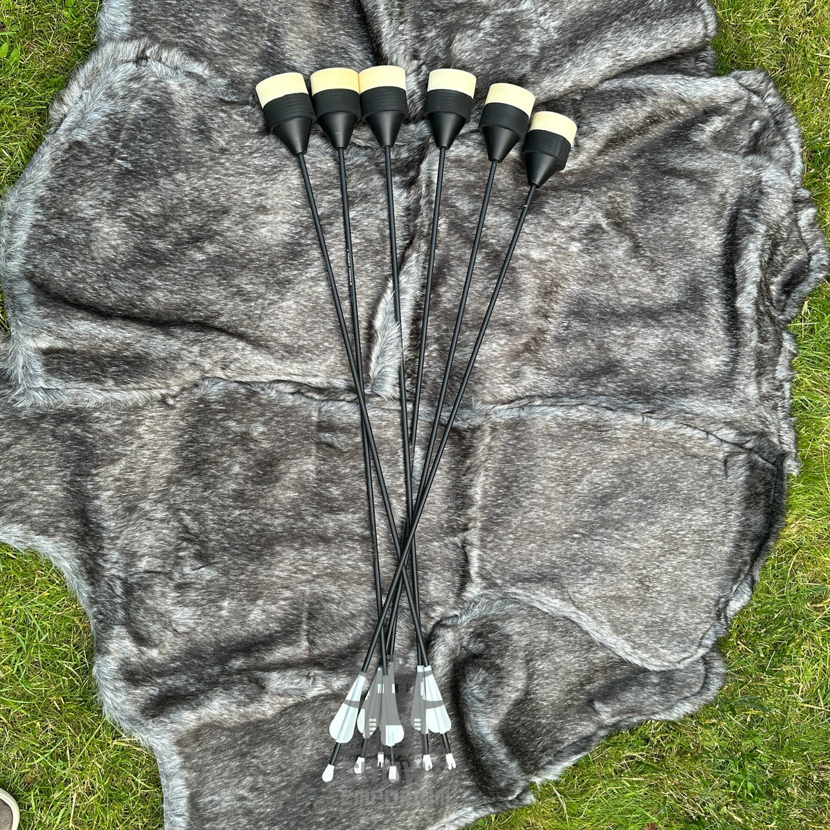 Set of black archery arrows with white nocks on a grey fabric background.