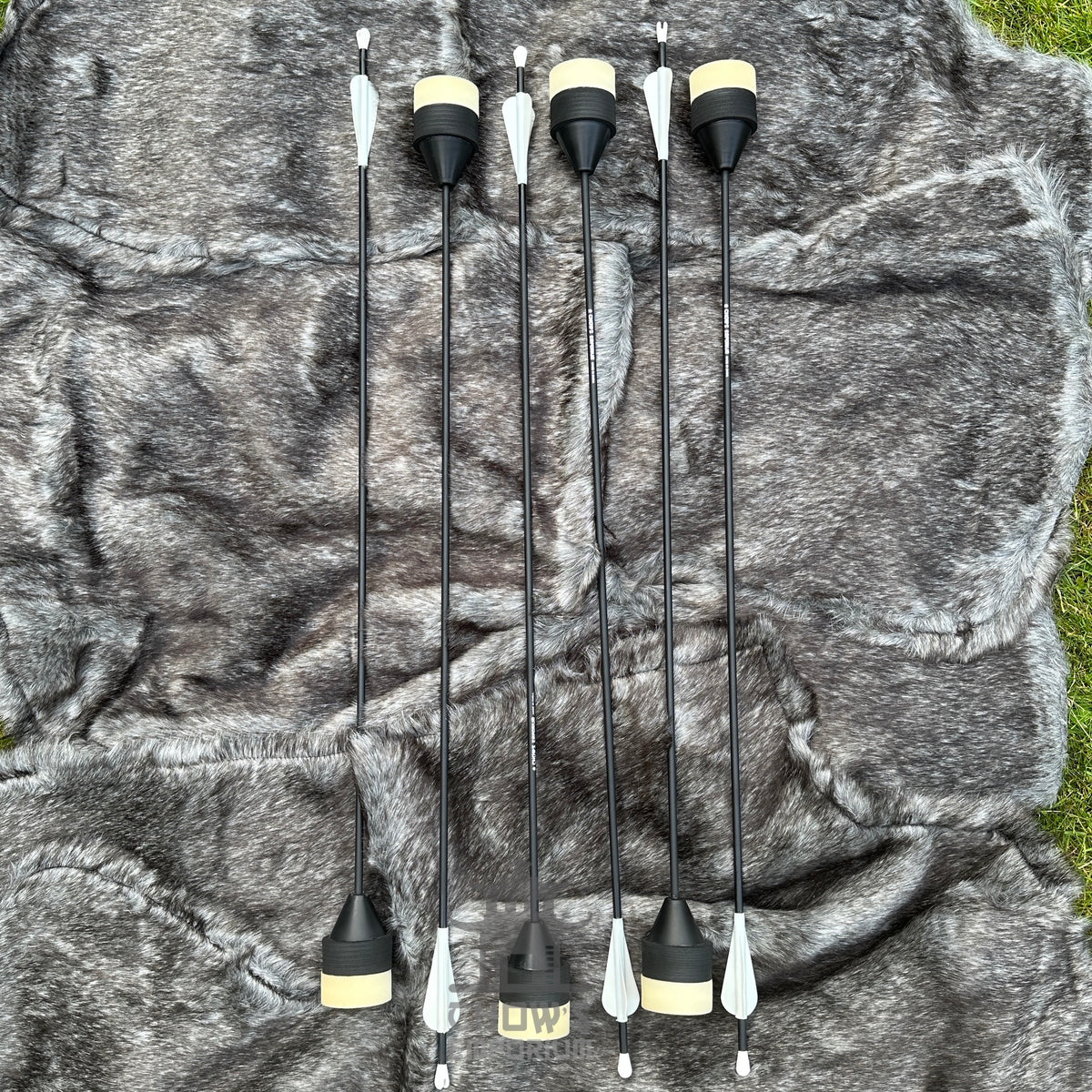 Set of six black and white archery nocks on a camouflage-patterned background.