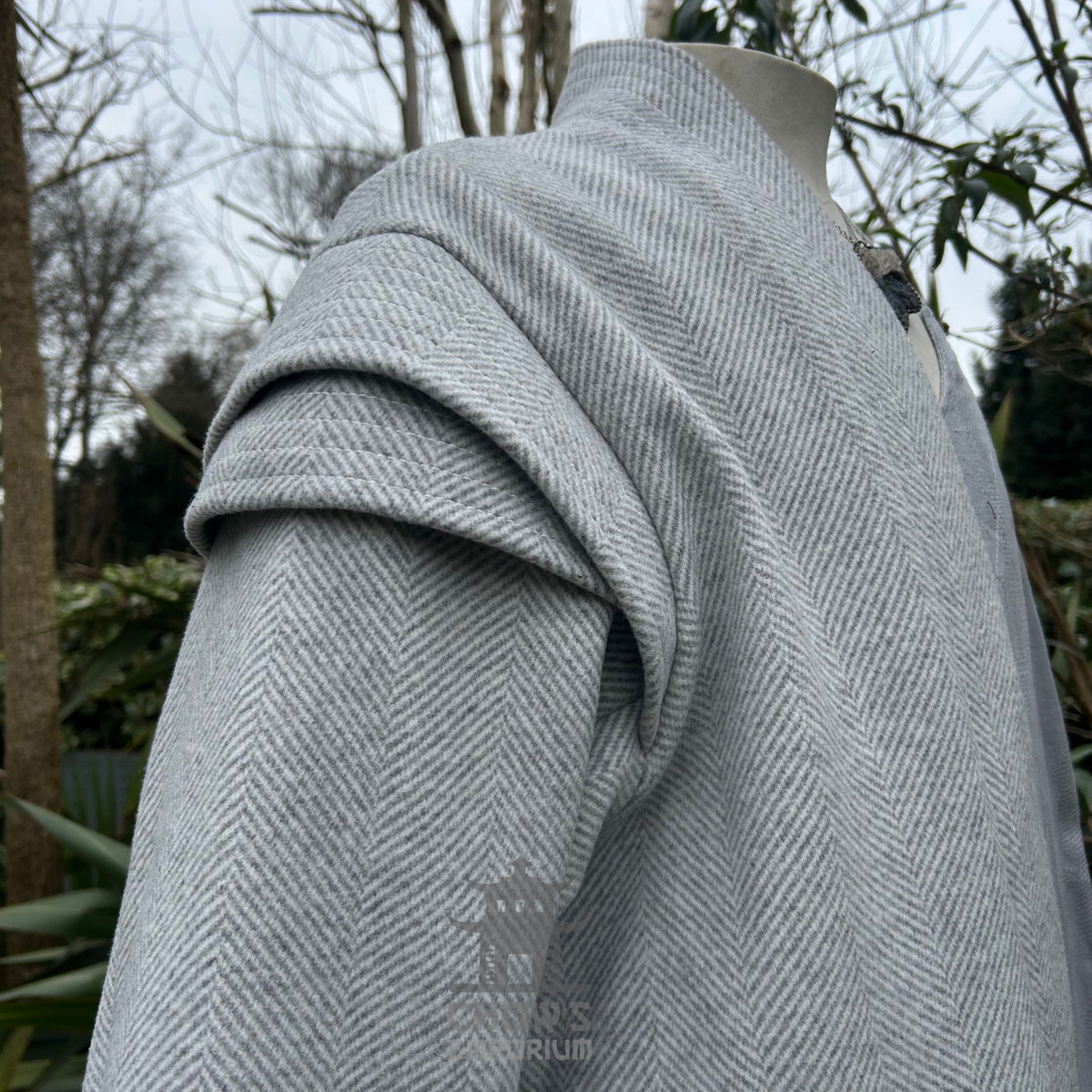 Close-up of herringbone fabric and stitching on light grey medieval LARP robe, textured fantasy.