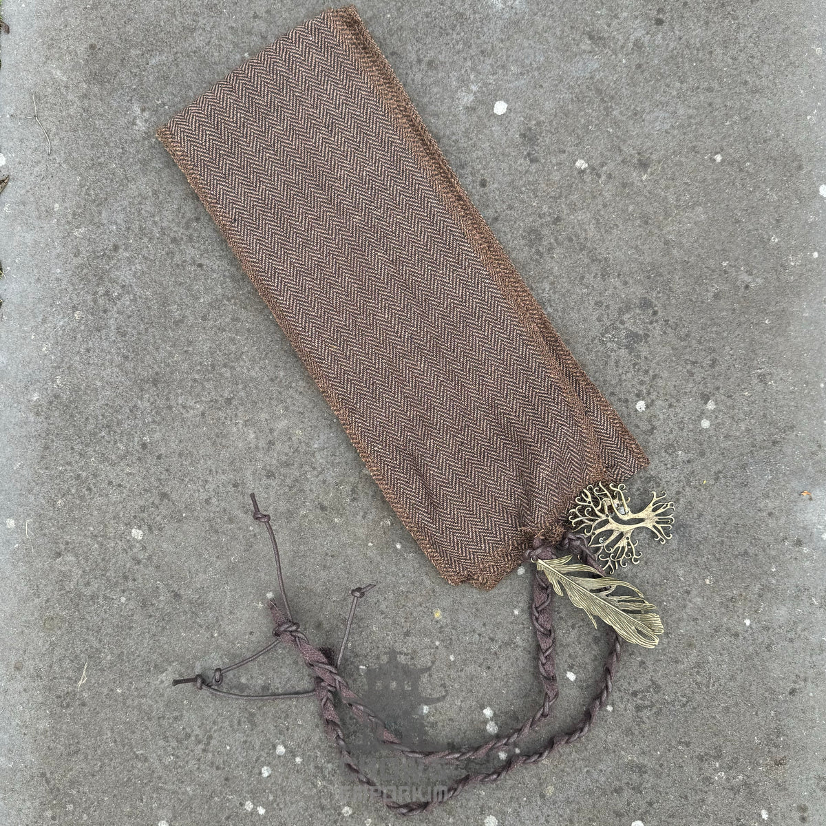 Brown herringbone wrap with braided ties on textured surface, medieval LARP accessory.