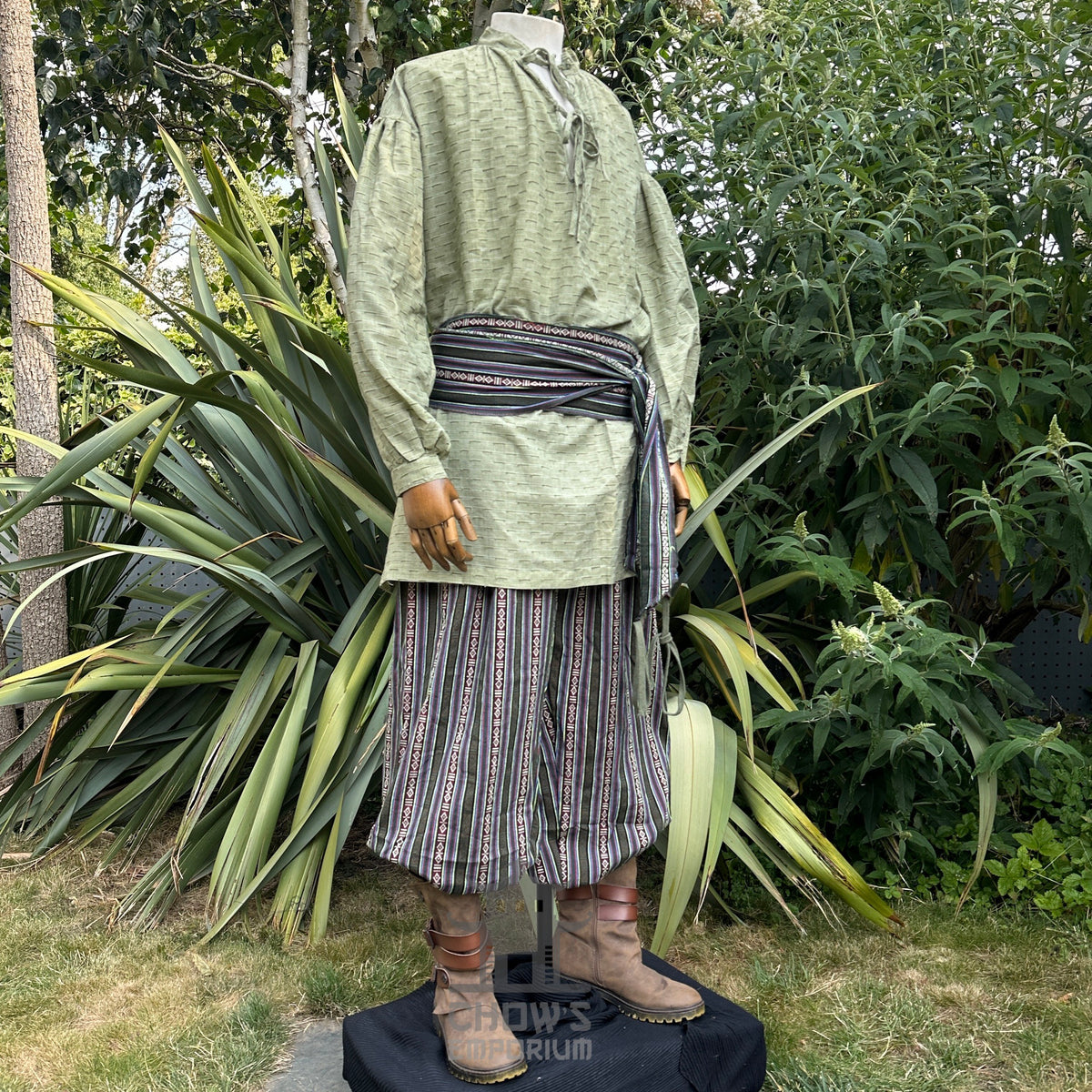 Medieval LARP outfit side view, featuring a green shirt, patterned trousers, matching sash.