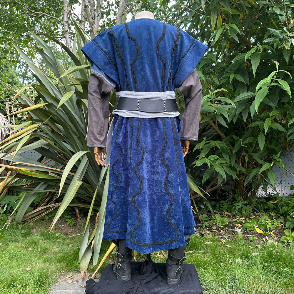 Medieval LARP costume back view, featuring a blue suede-effect panel waistcoat, two-tone cotton tunic and wool sash. For Renaissance Faire and historical roleplay events.