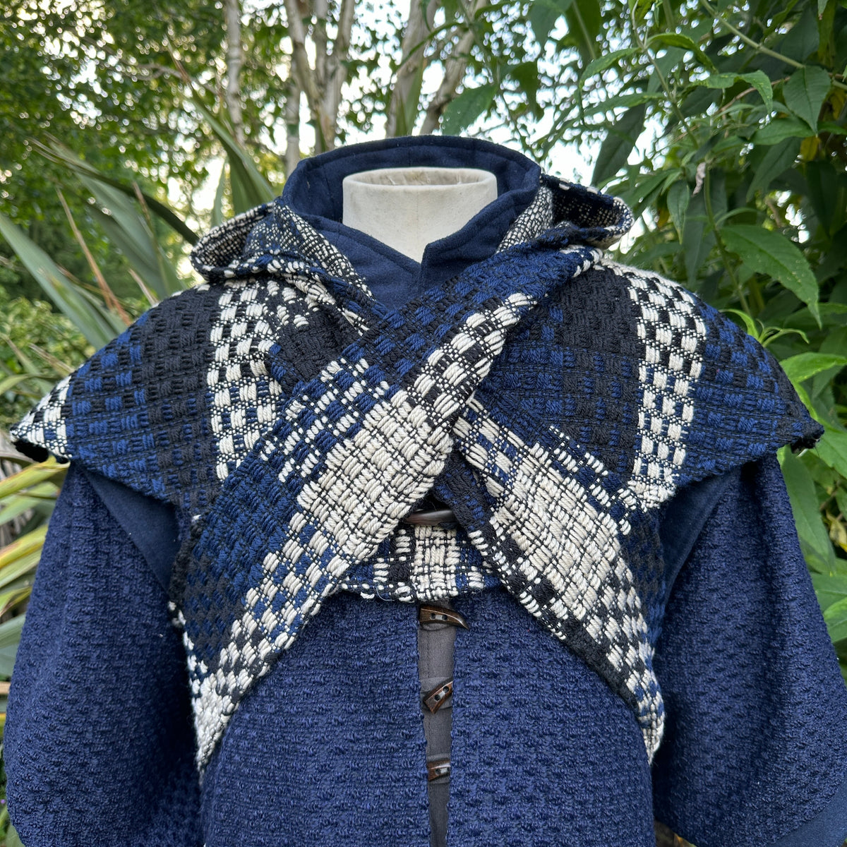 Blue and white check wool scarf hood for LARP, front view against greenery.