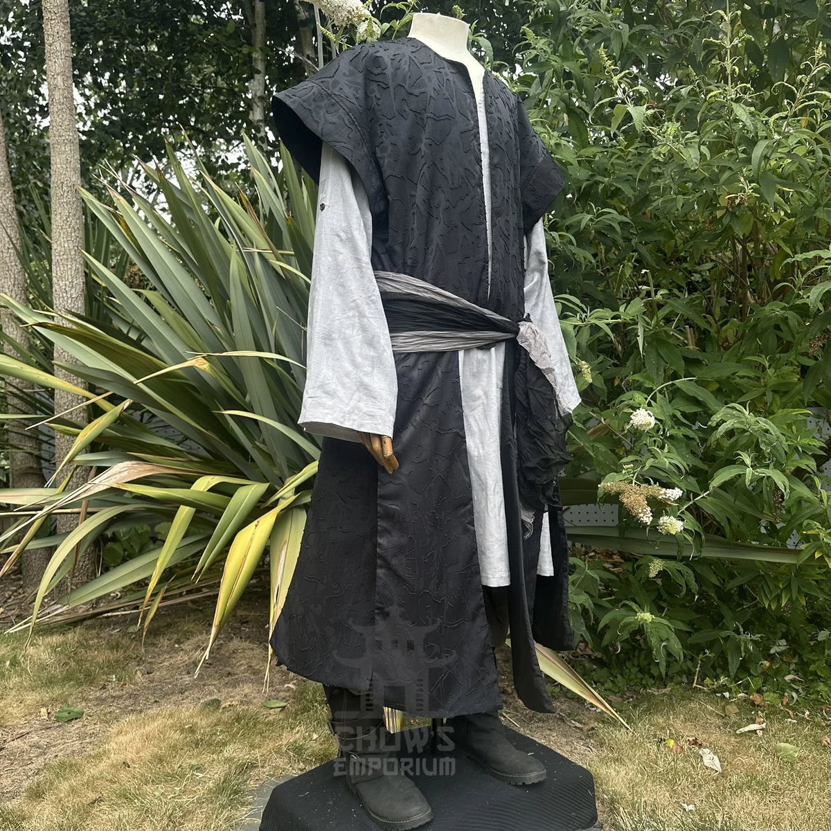 Black panelled waistcoat worn open with a sash draped at the waist, hood down, front view. Shirt and sash sold separately.