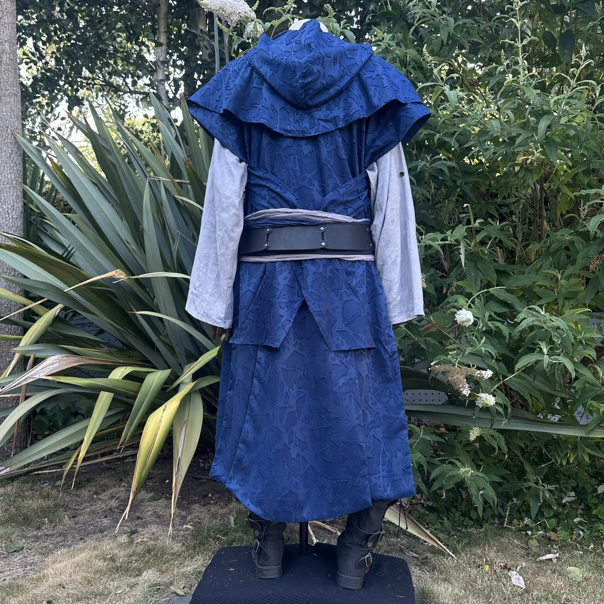 Blue panelled waistcoat and hood set, hood up with the ends draped as a cape across the shoulders, back view. Belt sold separately.