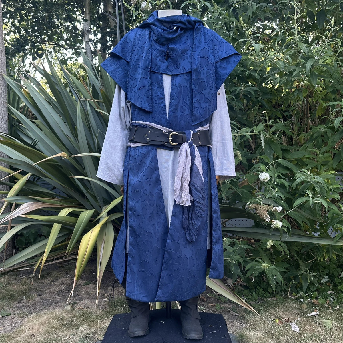 Close front view of the blue panelled waistcoat with the hood collar stood at the neck and a belt at the waist. Shirt and belt sold separately.
