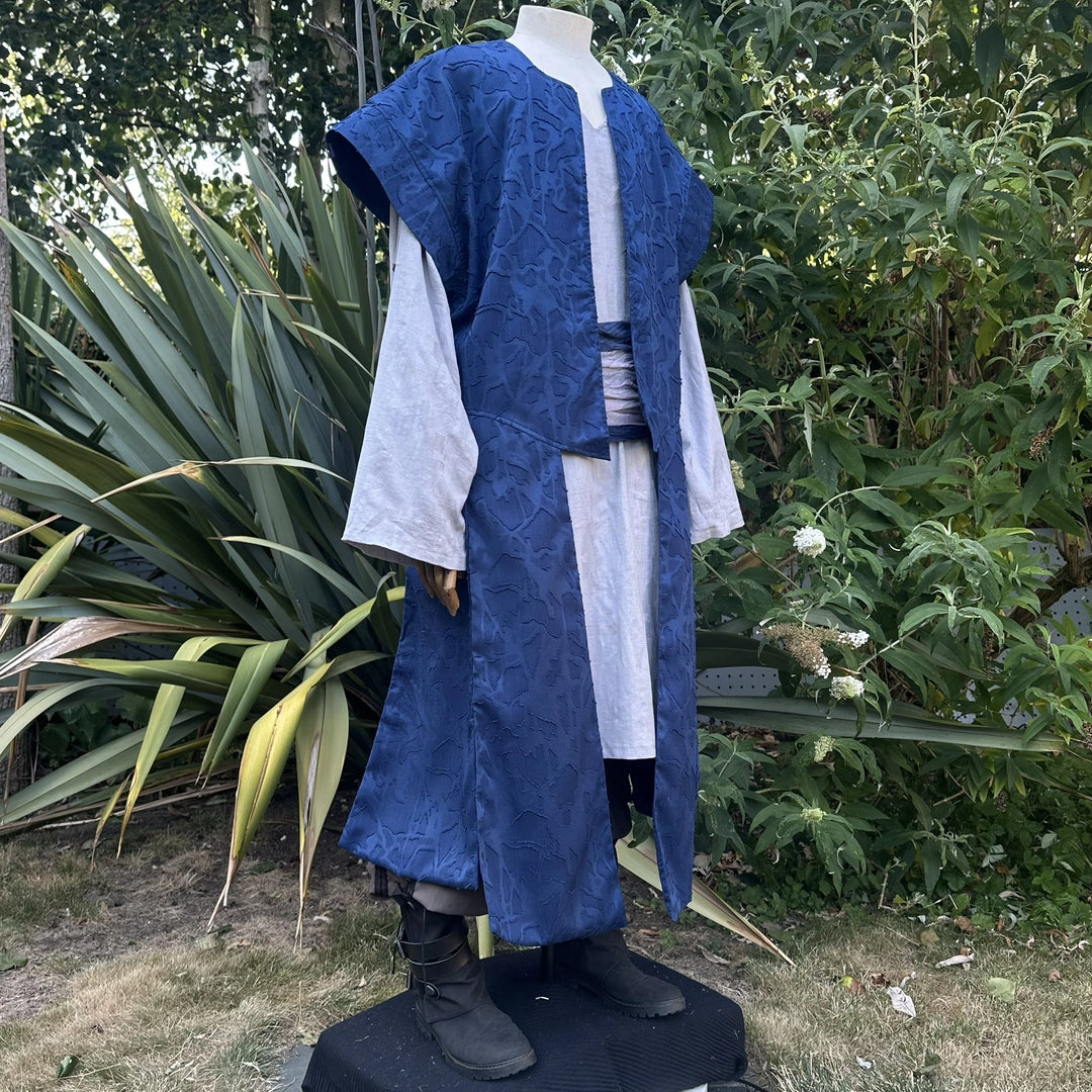 Blue panelled waistcoat worn open over a shirt with a sash at the waist, hood down, three-quarter view. Shirt and sash sold separately.