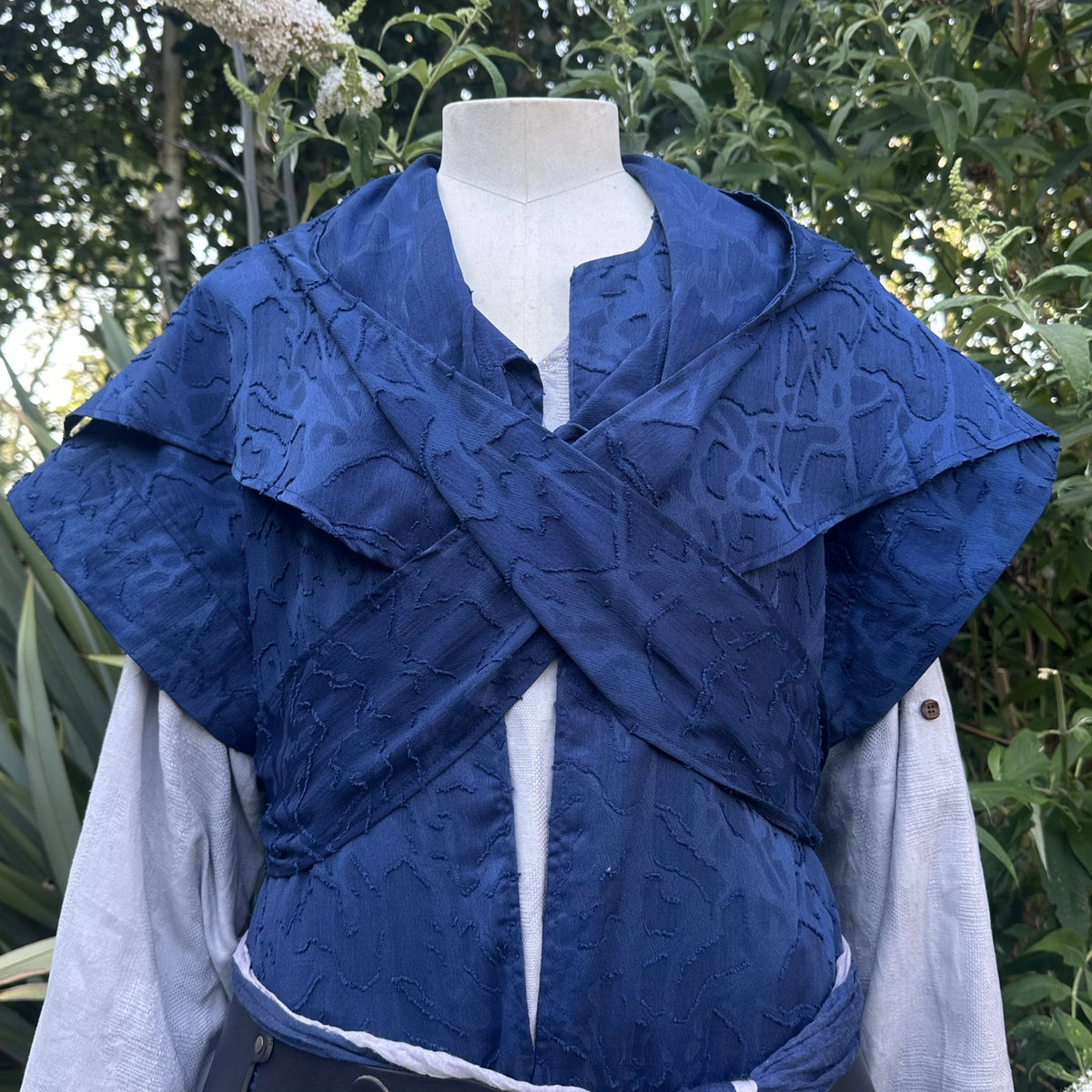 Close detail of the distressed blue panelling across the chest of the waistcoat and hood set.