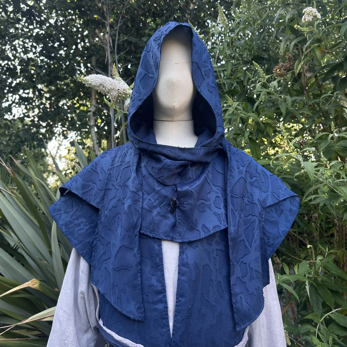 Close view of the blue scarf hood worn up with the collar stood at the neck, shown with the waistcoat.