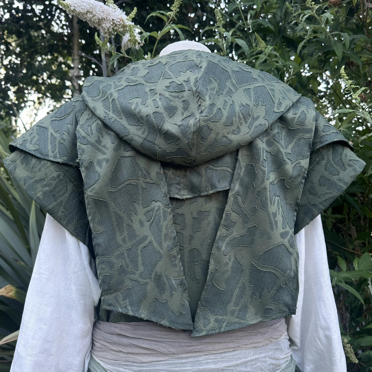 Green panelled waistcoat and hood set, hood up with the ends draped as a cape across the shoulders, back view. Belt sold separately.