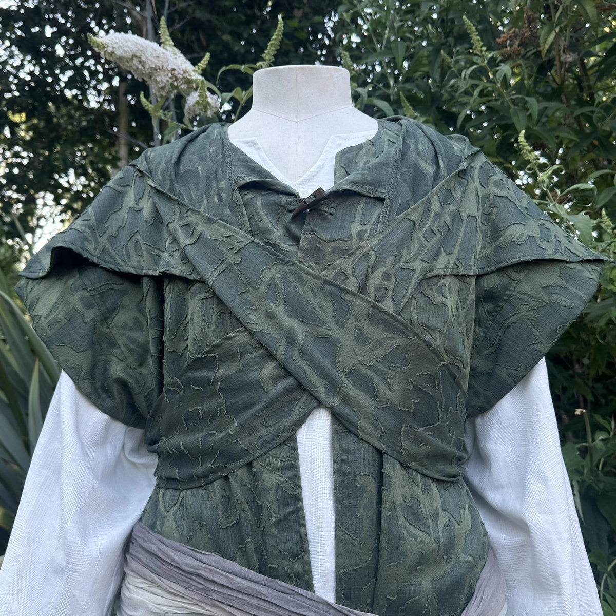 Close detail of the distressed green panelling across the chest of the waistcoat and hood set.
