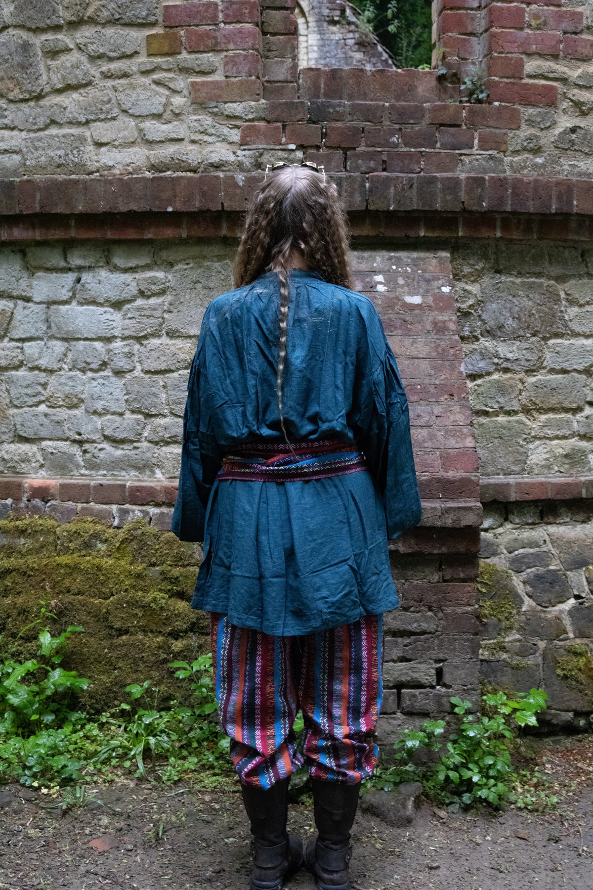 Back view of LARP druid set, teal robe, striped trousers, brick wall background.
