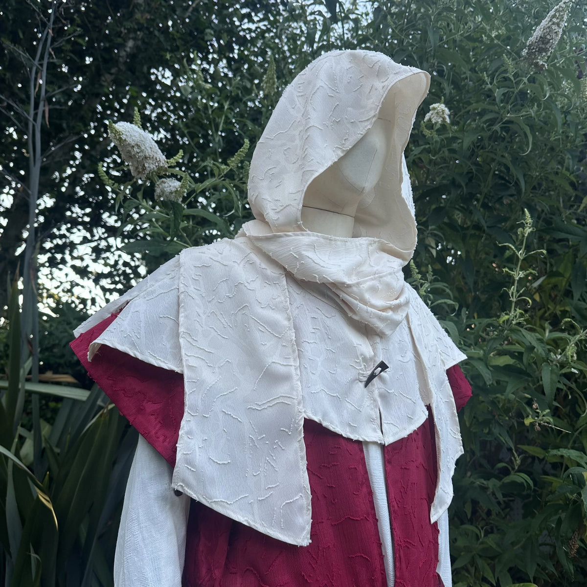 Cream hood worn up over red, three-quarter view showing the drape at the shoulder.