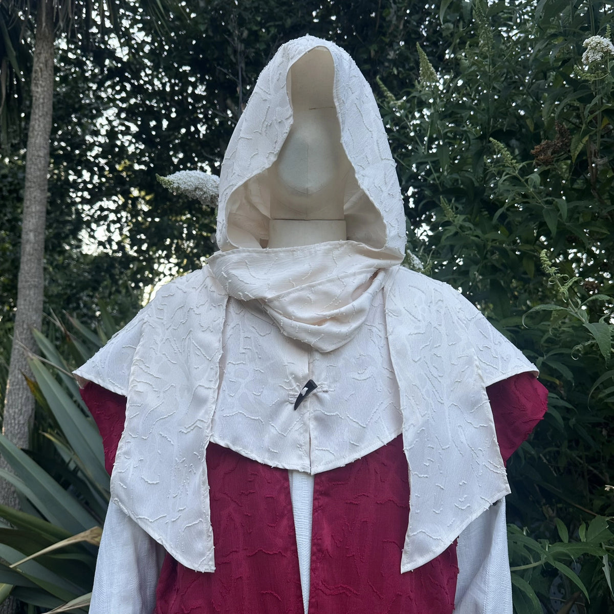 Close view of the cream hood worn up over the red layer at the neck and shoulders.