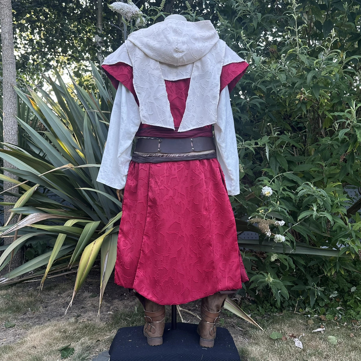 Cream hood and waistcoat over red, hood up and belted, back view. Belt sold separately.