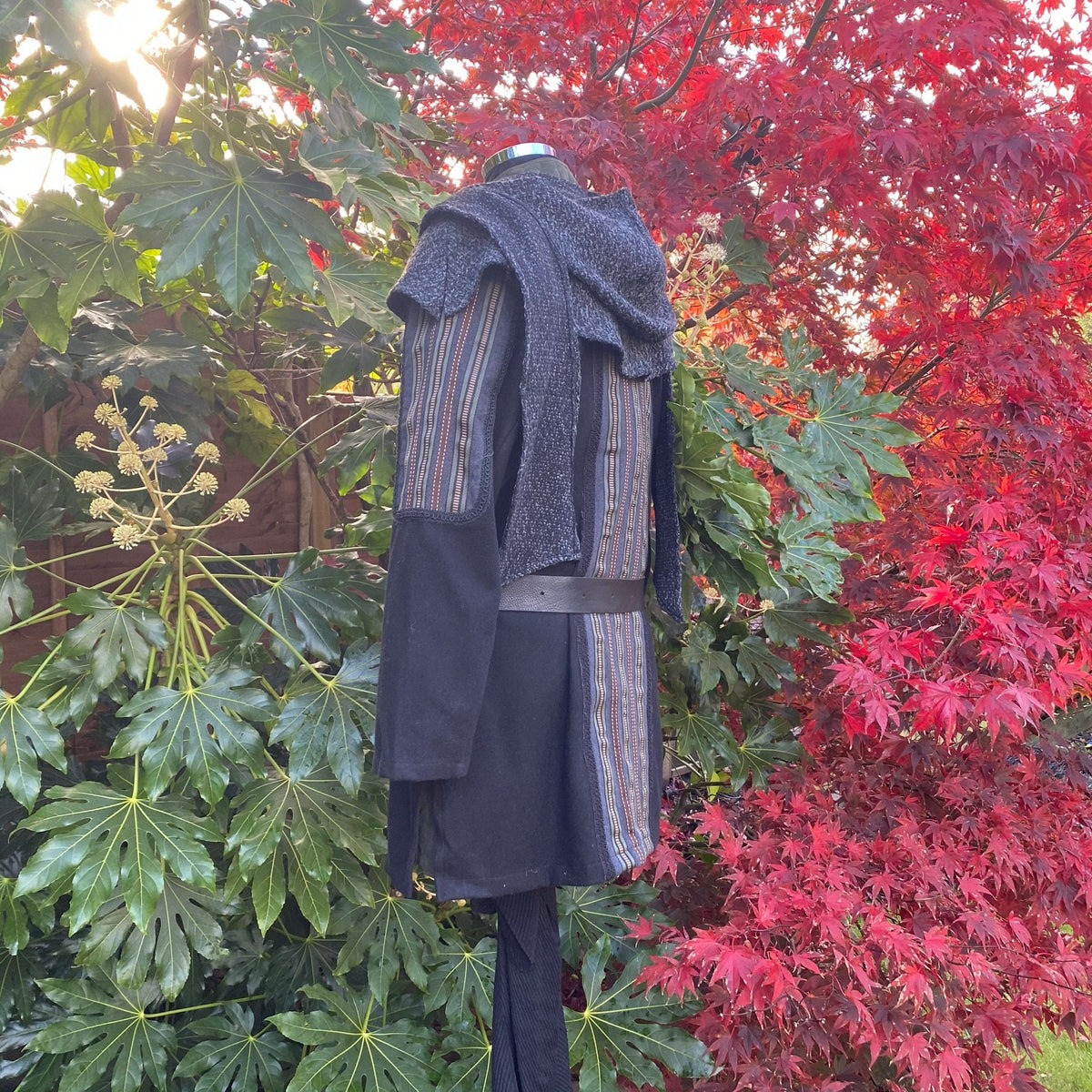 Side view of LARP ocean druid tunic; grey hood, colourful stripes, forest backdrop.