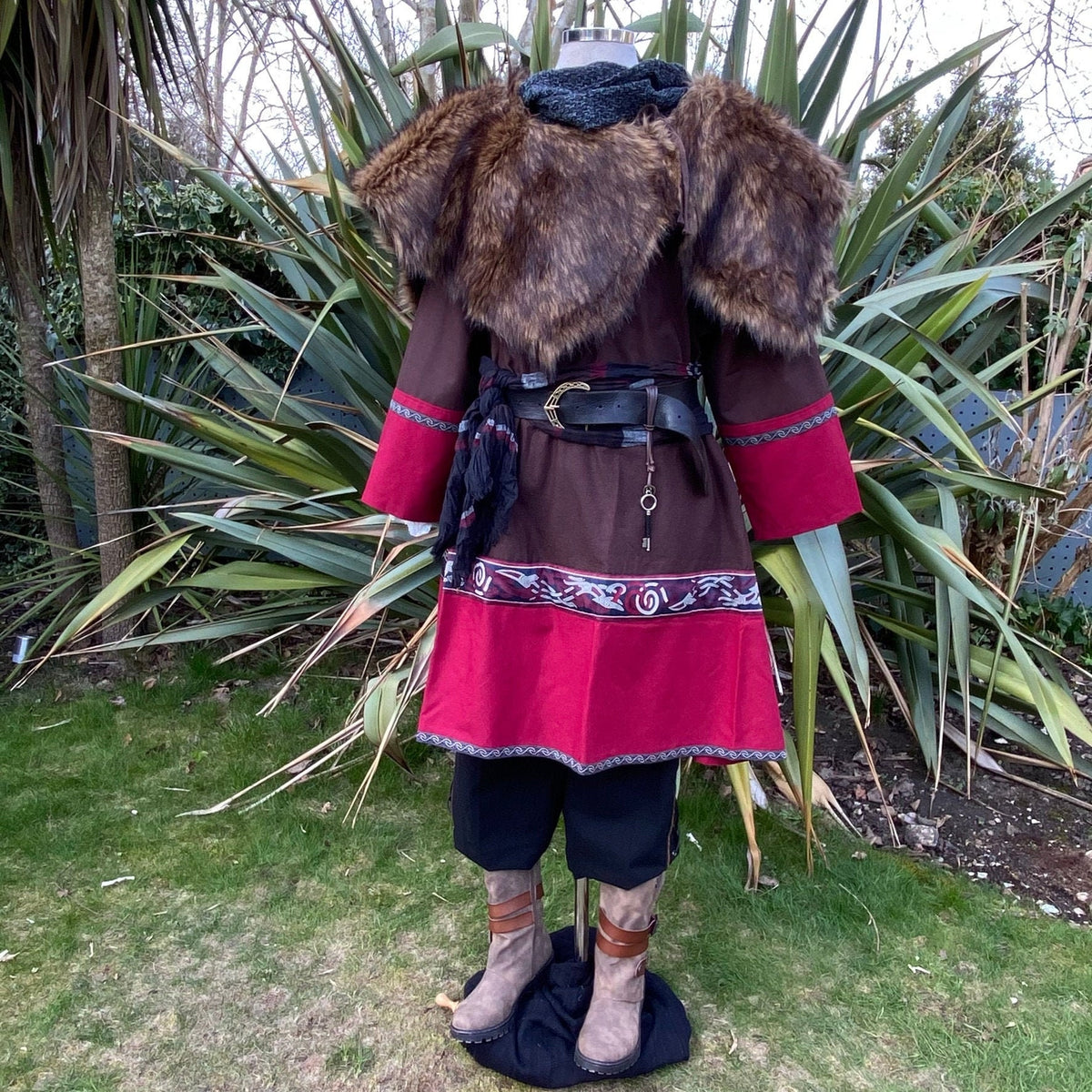 LARP outfit front view: brown tunic, red accents, faux fur mantle, nature backdrop.