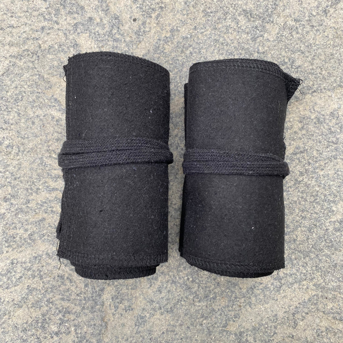 Two rolled black wool leg wraps on stone for medieval LARP.