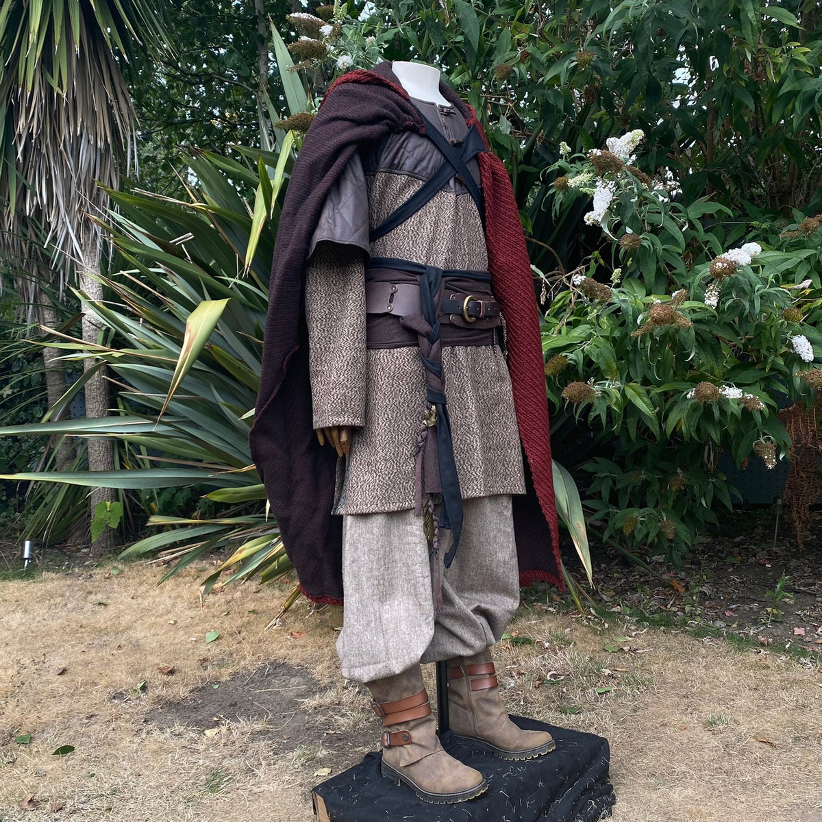 LARP outfit front view: textured tunic, red cloak, natural setting.