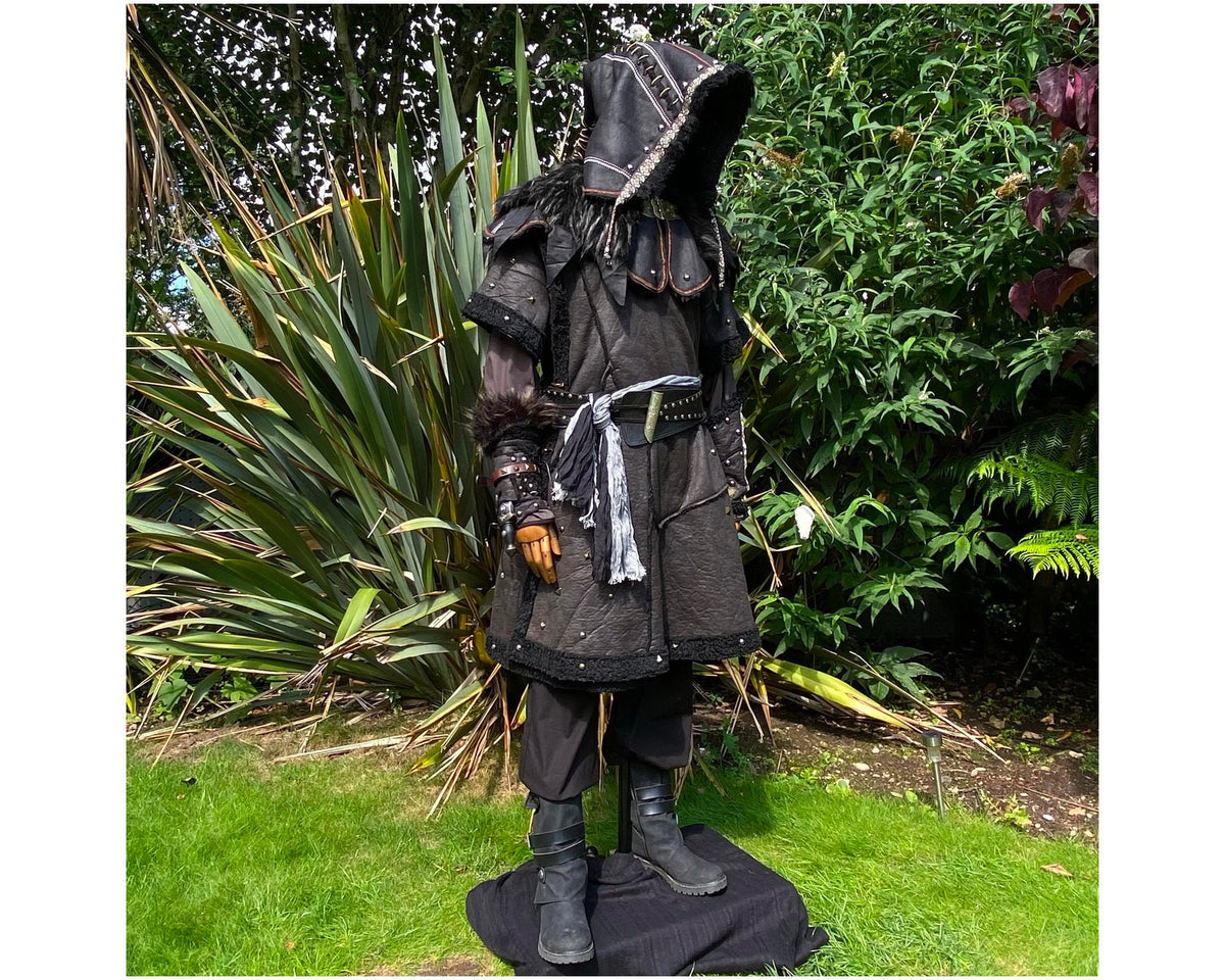 Medieval LARP costume side view featuring a black faux leather tunic, hood, vambraces, shirt.