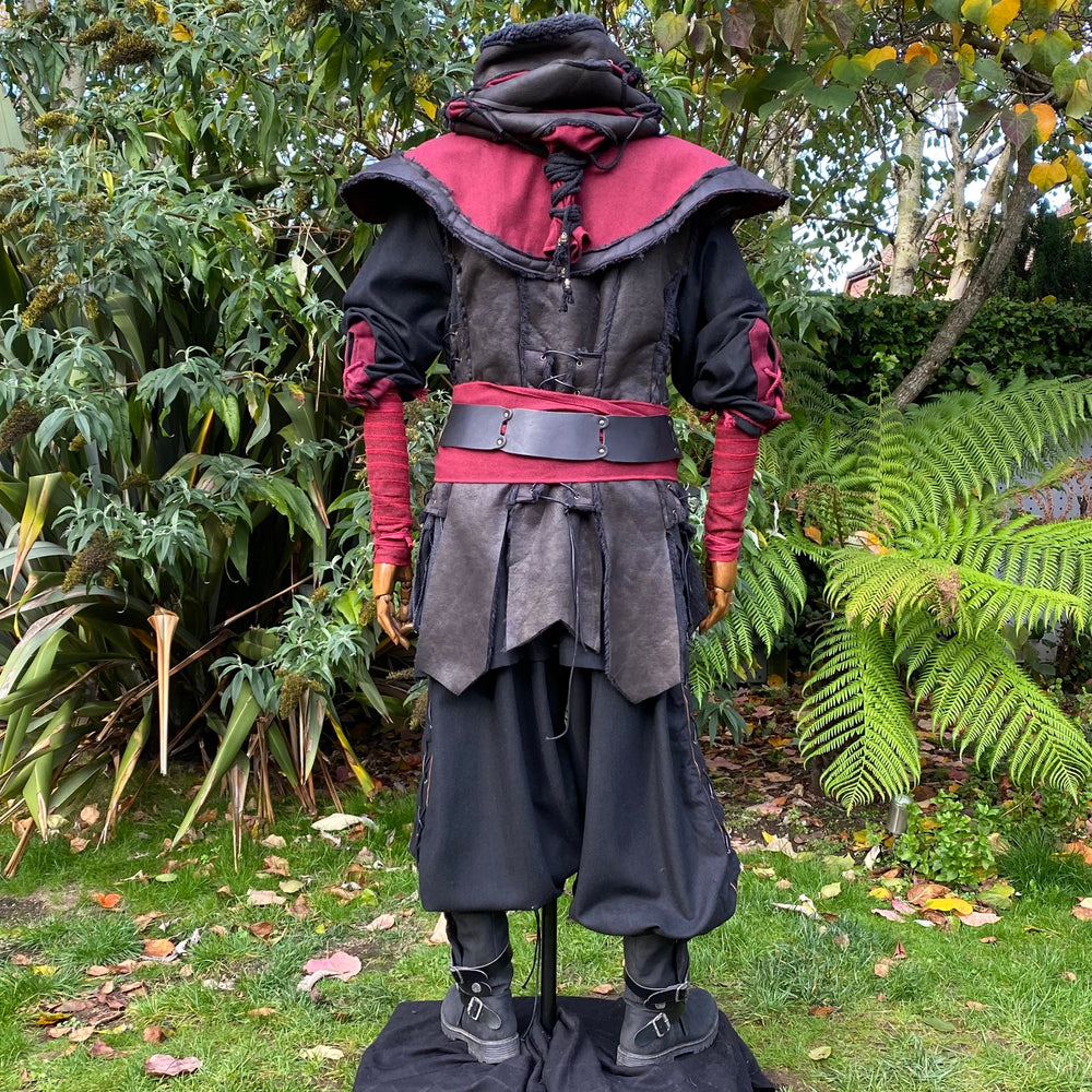 Medieval LARP outfit back view, featuring a red and black hood, waistcoat, shirt, and sash. For Renaissance Faire and historical roleplay events.