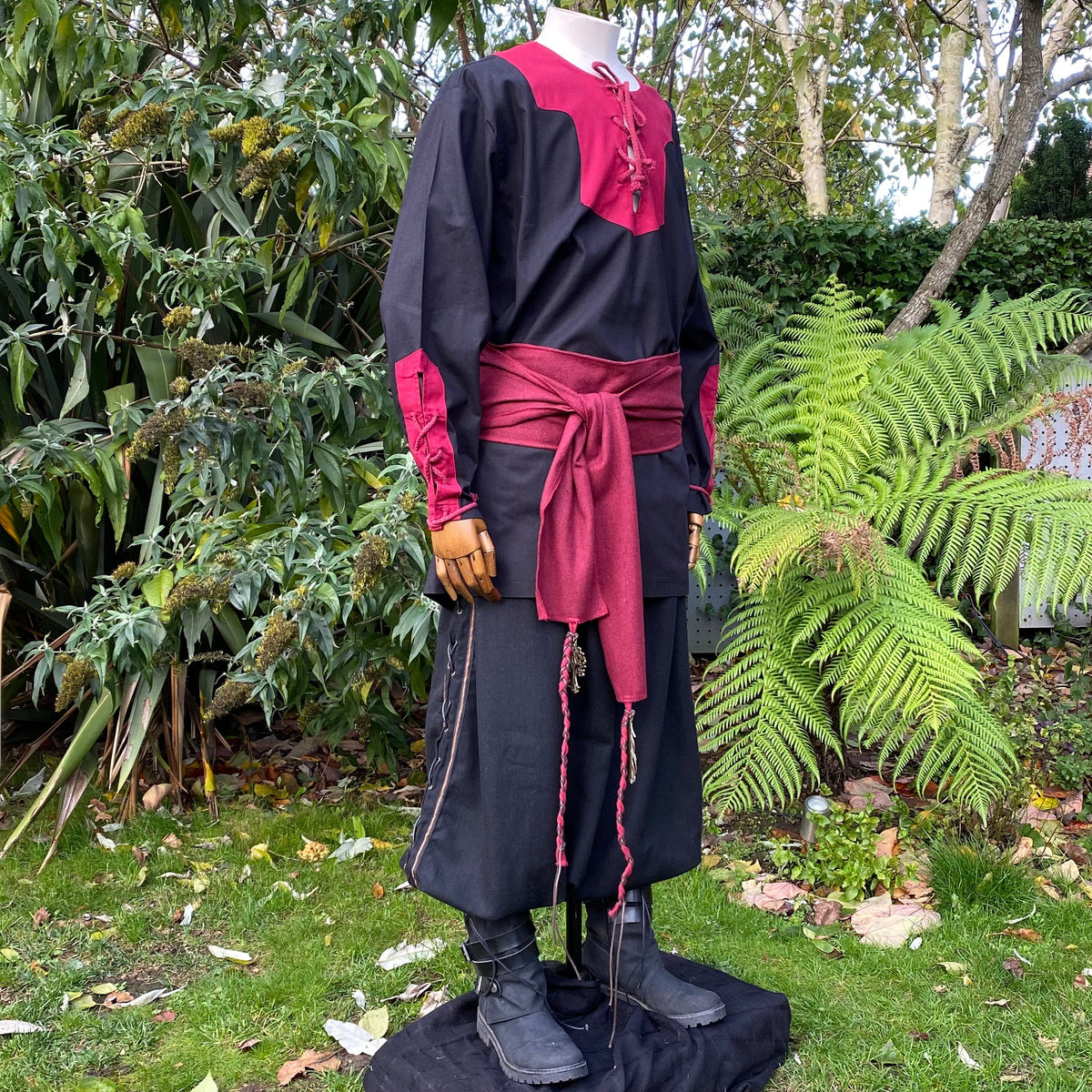 Medieval LARP outfit with red sash, outdoor garden setting, side view.