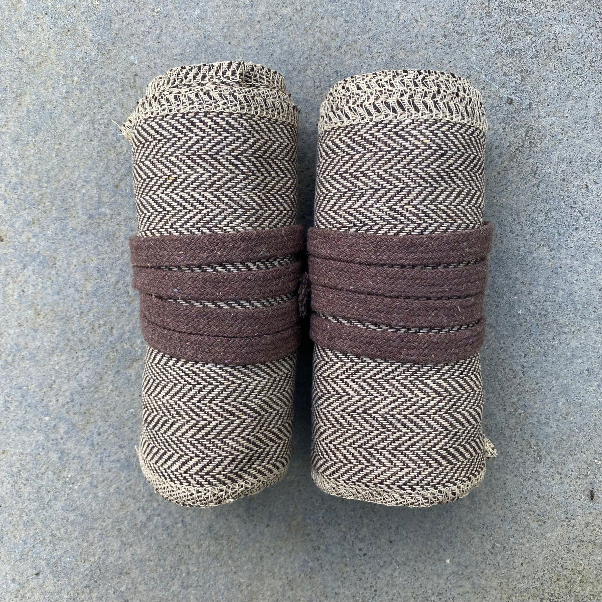 Rolled herringbone wool leg wraps for medieval LARP on grey surface.