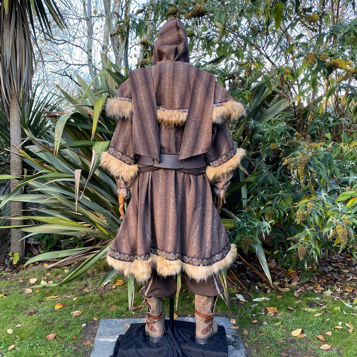 Brown LARP tunic and hood with fur trim, back view in greenery.