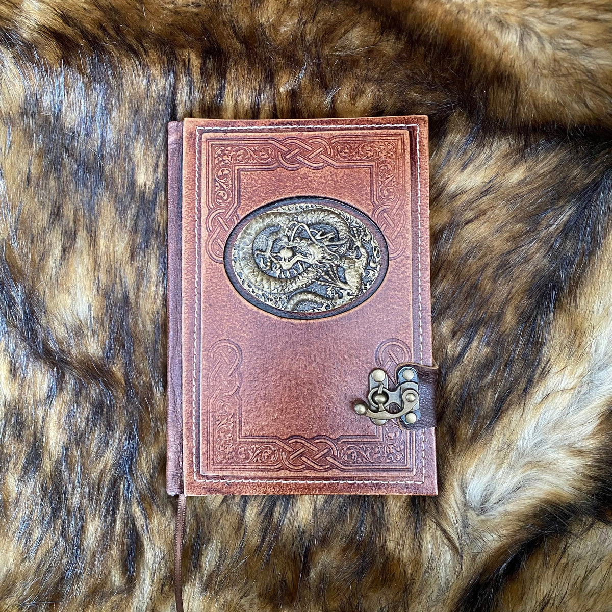 Brown leather journal with dragon emblem, clasp on fur; medieval LARP theme.
