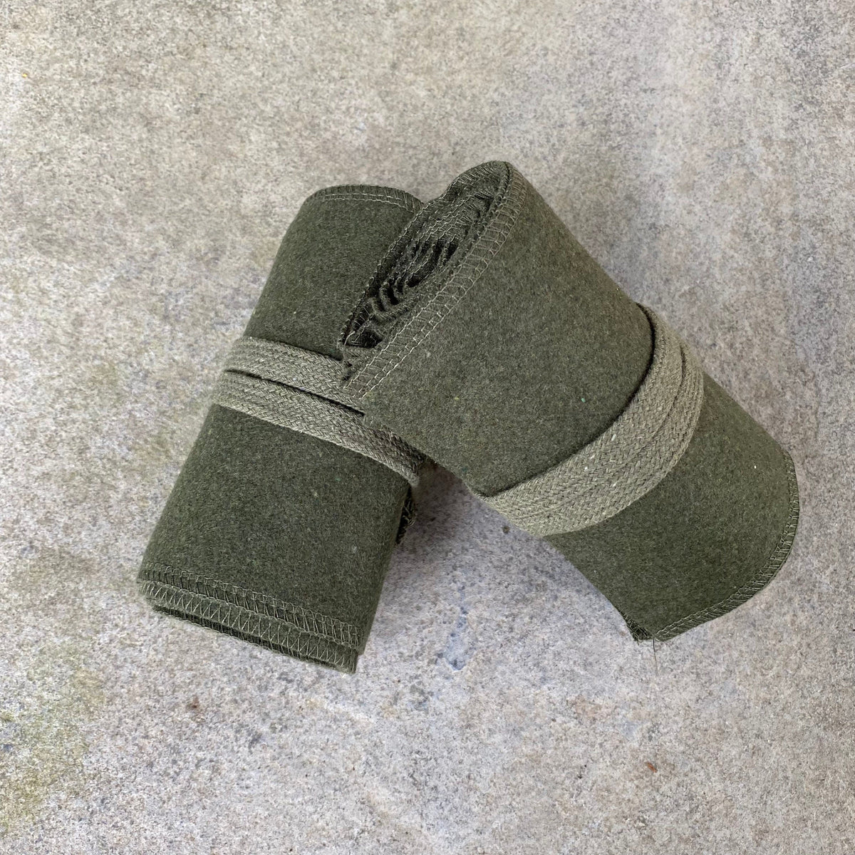 Two rolled dark green wool leg wraps on stone for LARP.