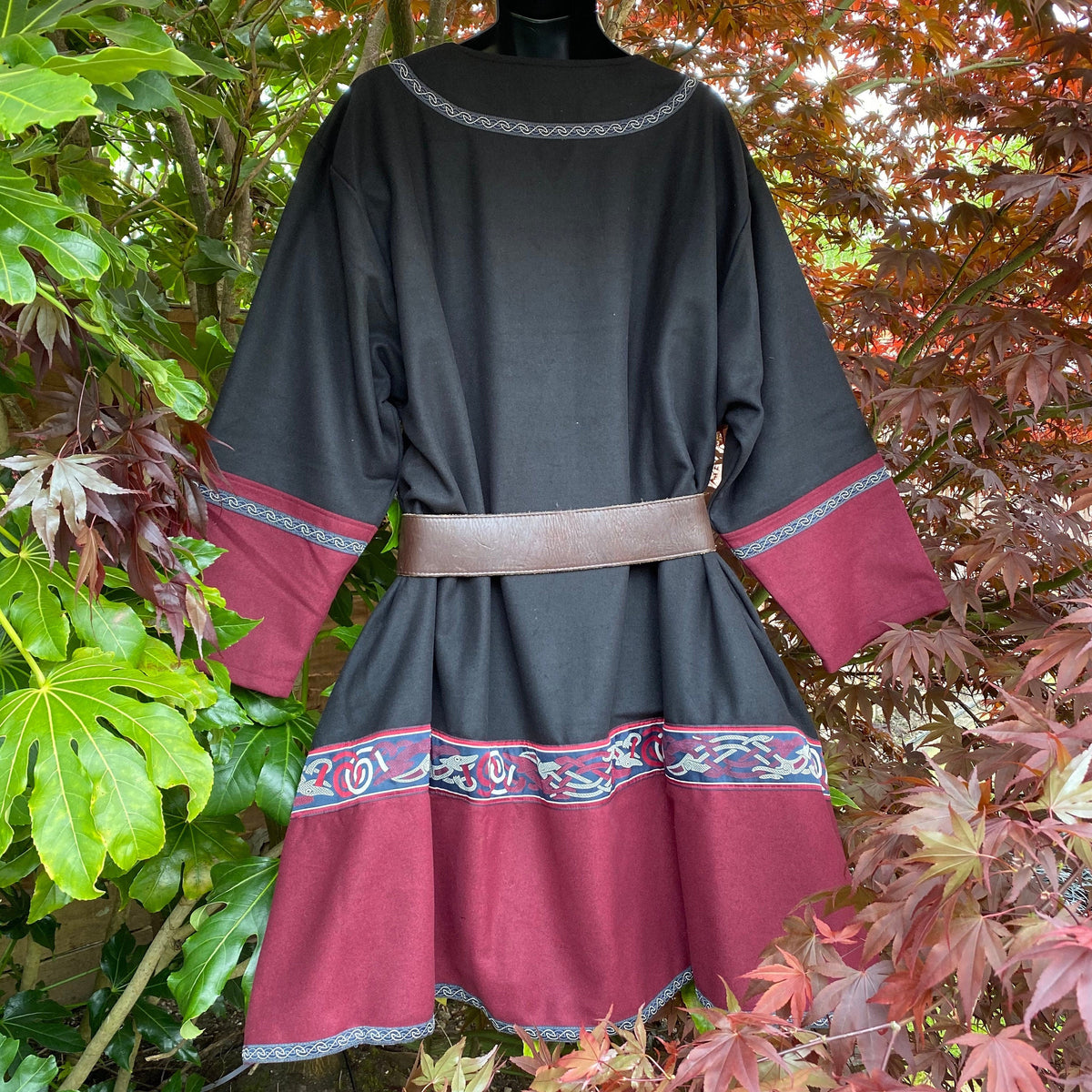 Rear view of LARP tunic, black and red with embroidery, amidst green leaves.