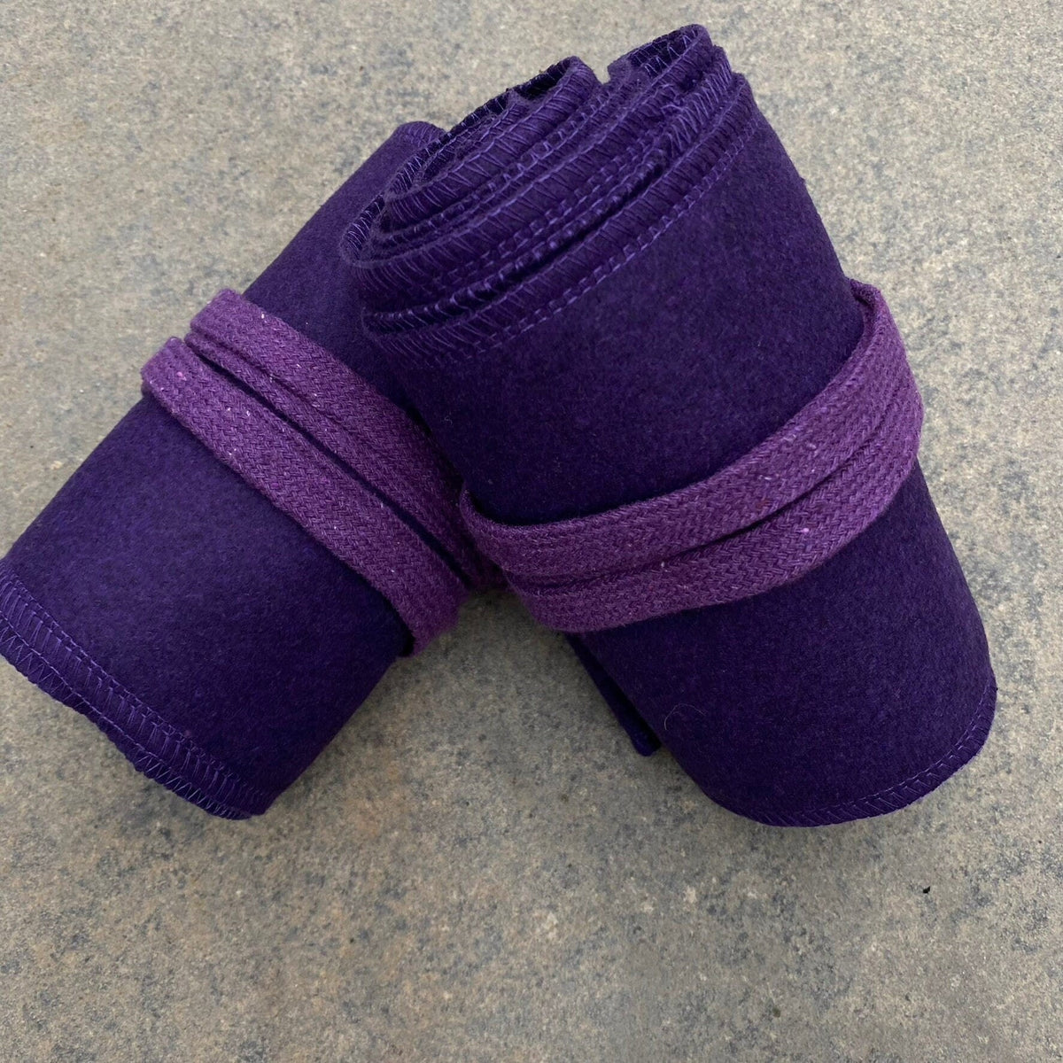 Rolled purple wool leg wraps for LARP, top view on stone surface.