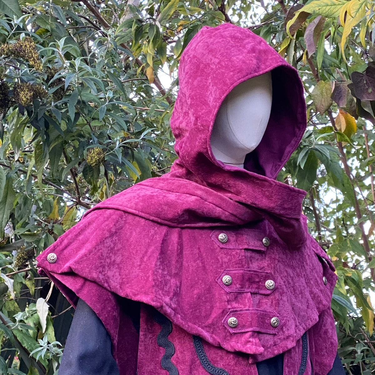 Crimson hooded LARP outfit with decorative buttons, forest backdrop.