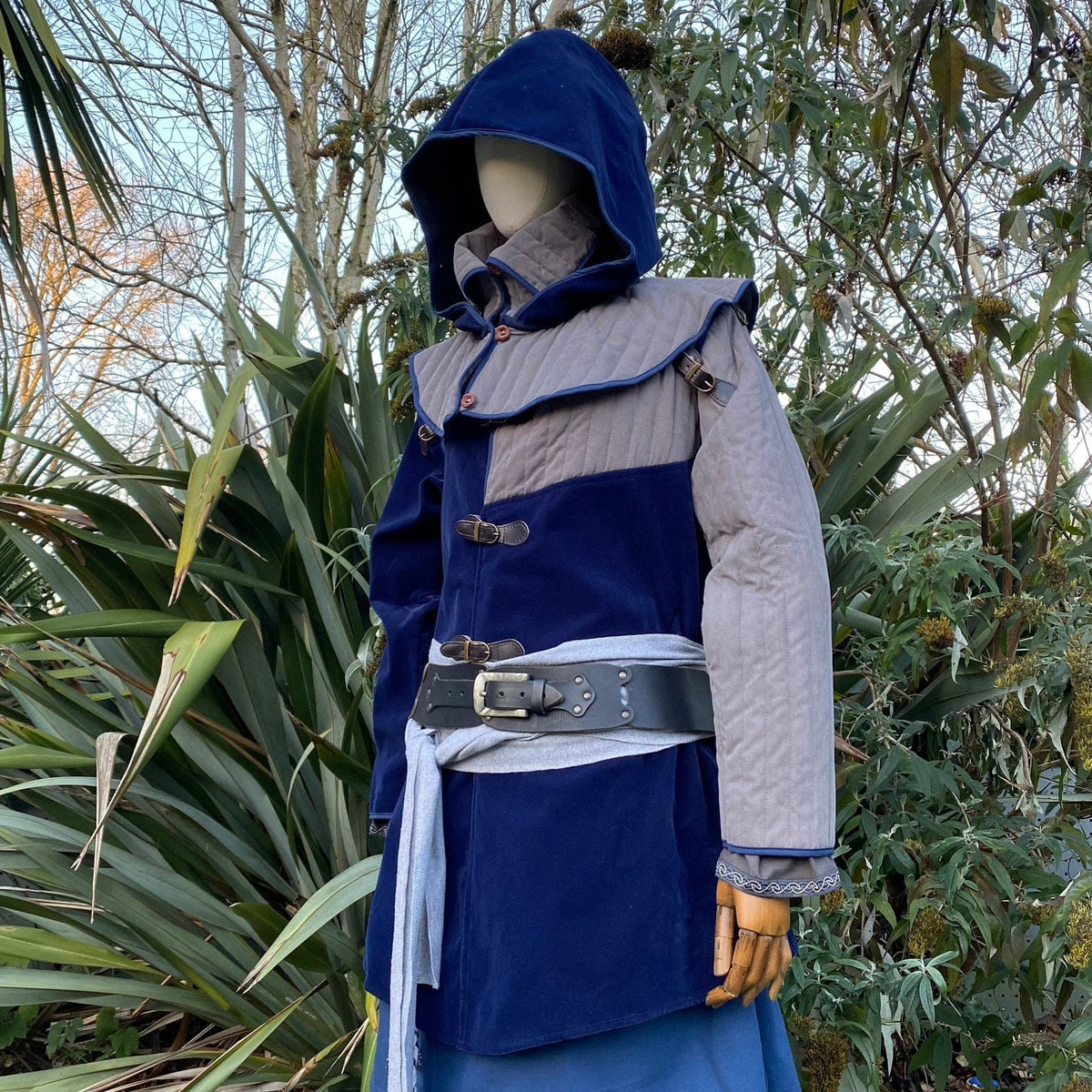 Medieval LARP hooded blue gambeson with belt, side forest background.