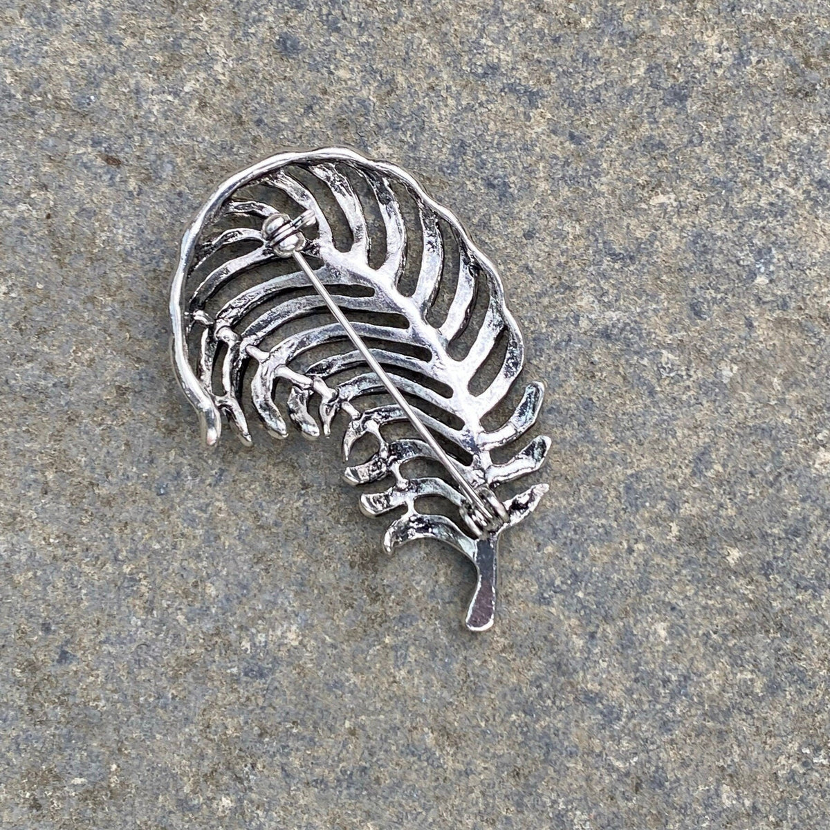 Dark silver fern-shaped brooch back view on stone for LARP.