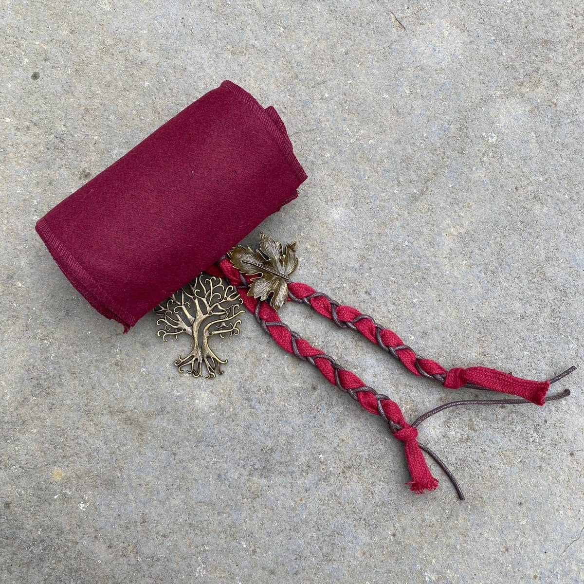 Braided red wool LARP sash with bronze leaf and tree accents on stone.