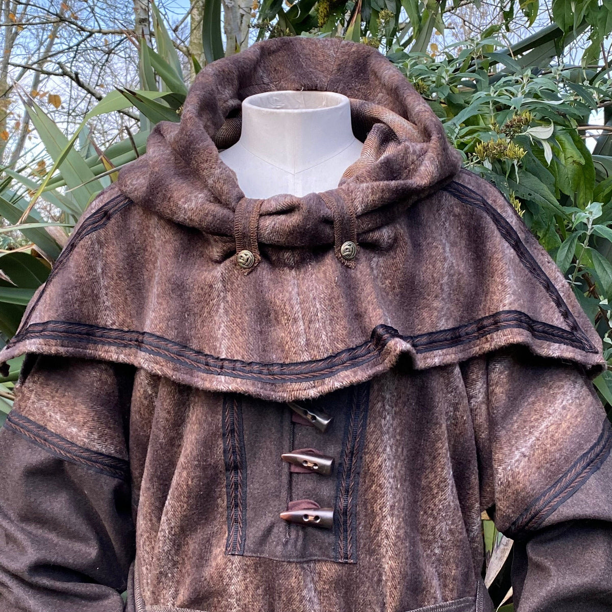 Brown wool LARP snood hood with toggle details, leafy backdrop.