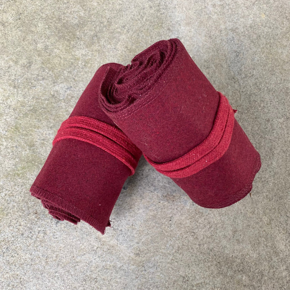 Rolled red wool leg wraps for medieval LARP against stone background.