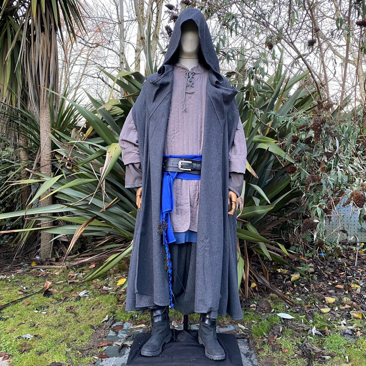 Hooded medieval LARP attire with blue sash, forest backdrop, front view.