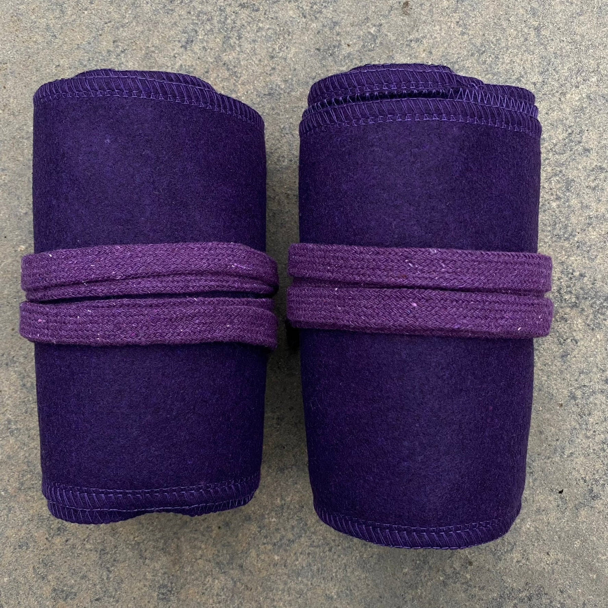 Purple wool leg wraps for LARP, rolled and tied on a stone surface.